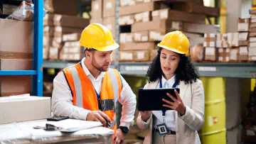 Two people in hard hats look at a clipboard