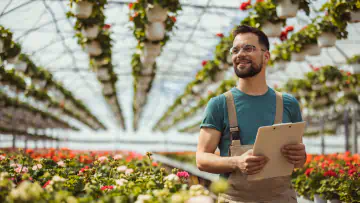 Man holding clipboard stands in greenhouse